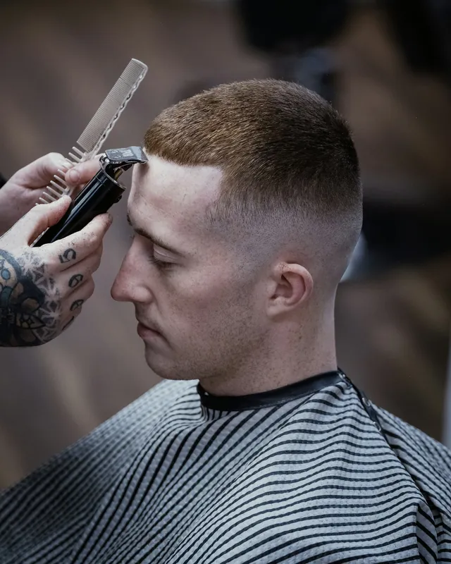Kapster merapikan crew cut pendek dengan mesin cukur