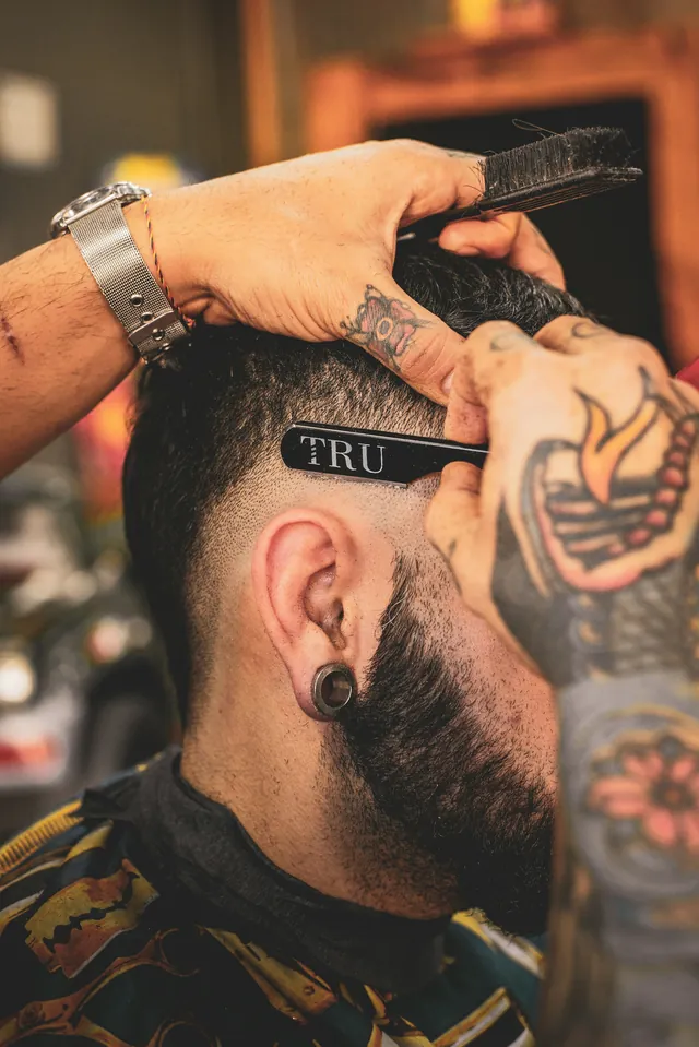 Kapster bertato merapikan garis skin fade dengan pisau cukur