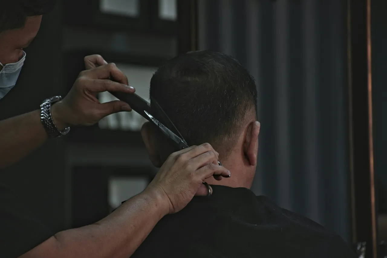 Kapster merapikan garis rambut belakang seorang pelanggan dengan pisau cukur